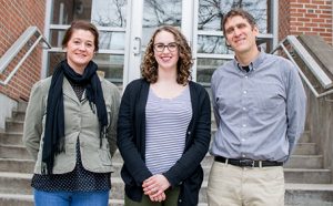 Katie Gold, Profs. Amanda Gevens and Phil Townsend standing in front of concrete stairs and glass doors in front of a brick building